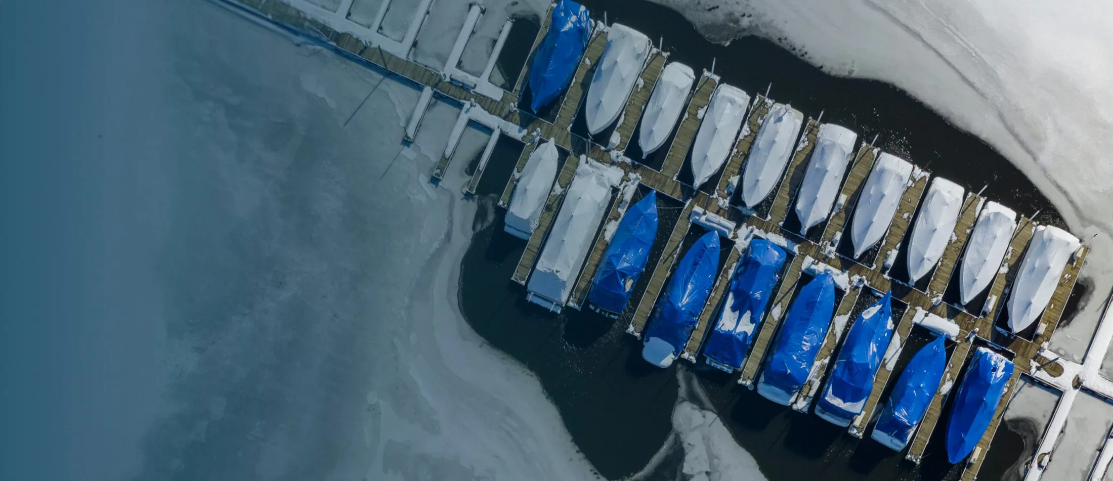 Aerial photograph of open water around marina slips surrounded by winter ice